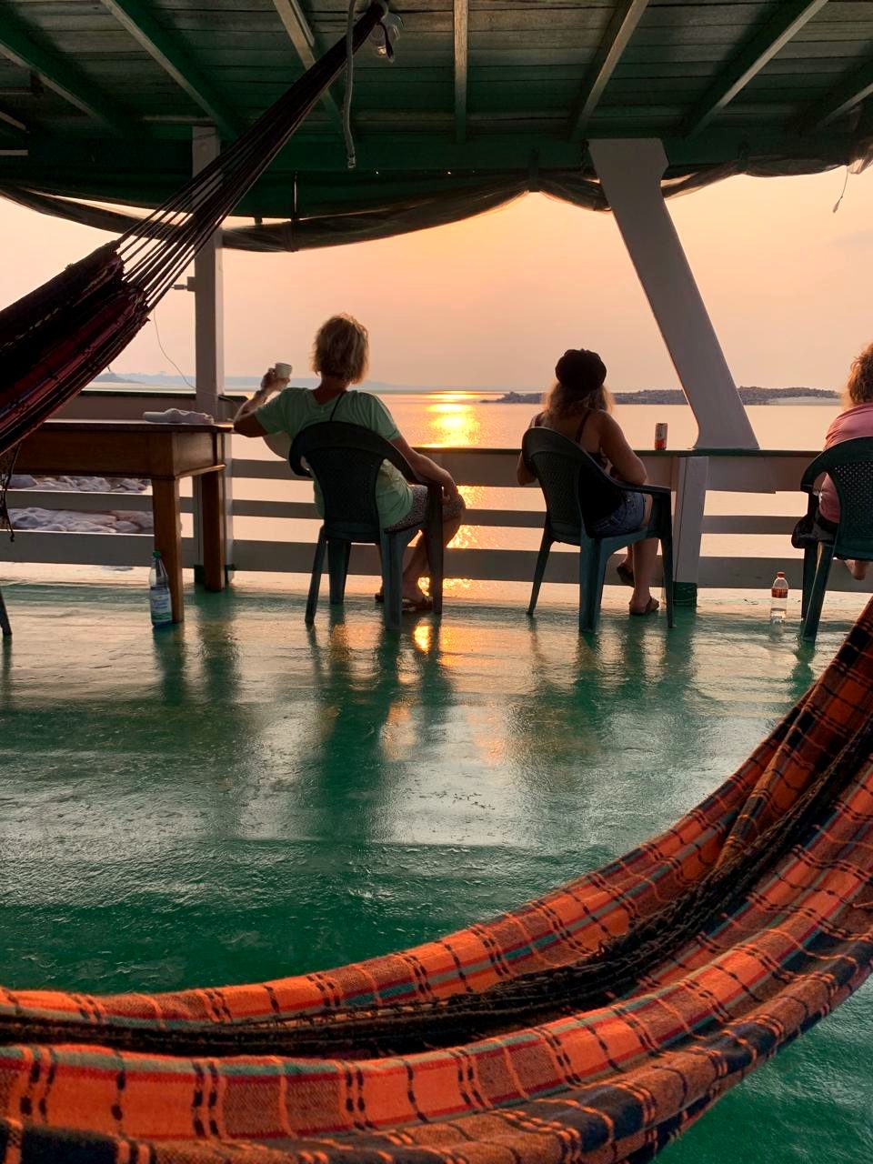 Viajantes vendo o pôr do sol no convés entre as redes